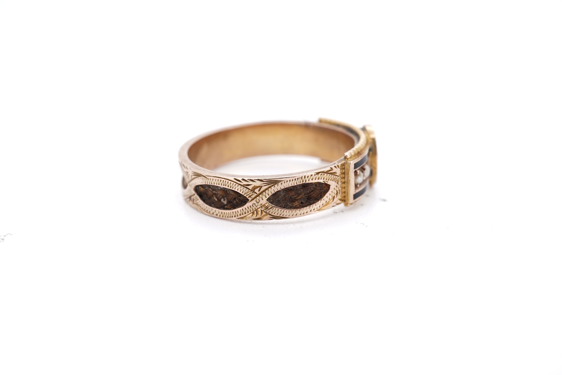 A George V 9ct gold, black enamel and seed pearl set mourning ring, the shank with panels of plaited hair, size O, gross weight 2.5 grams.